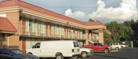 A motel with a red roof, multiple balconies, and a parking lot with several vehicles.