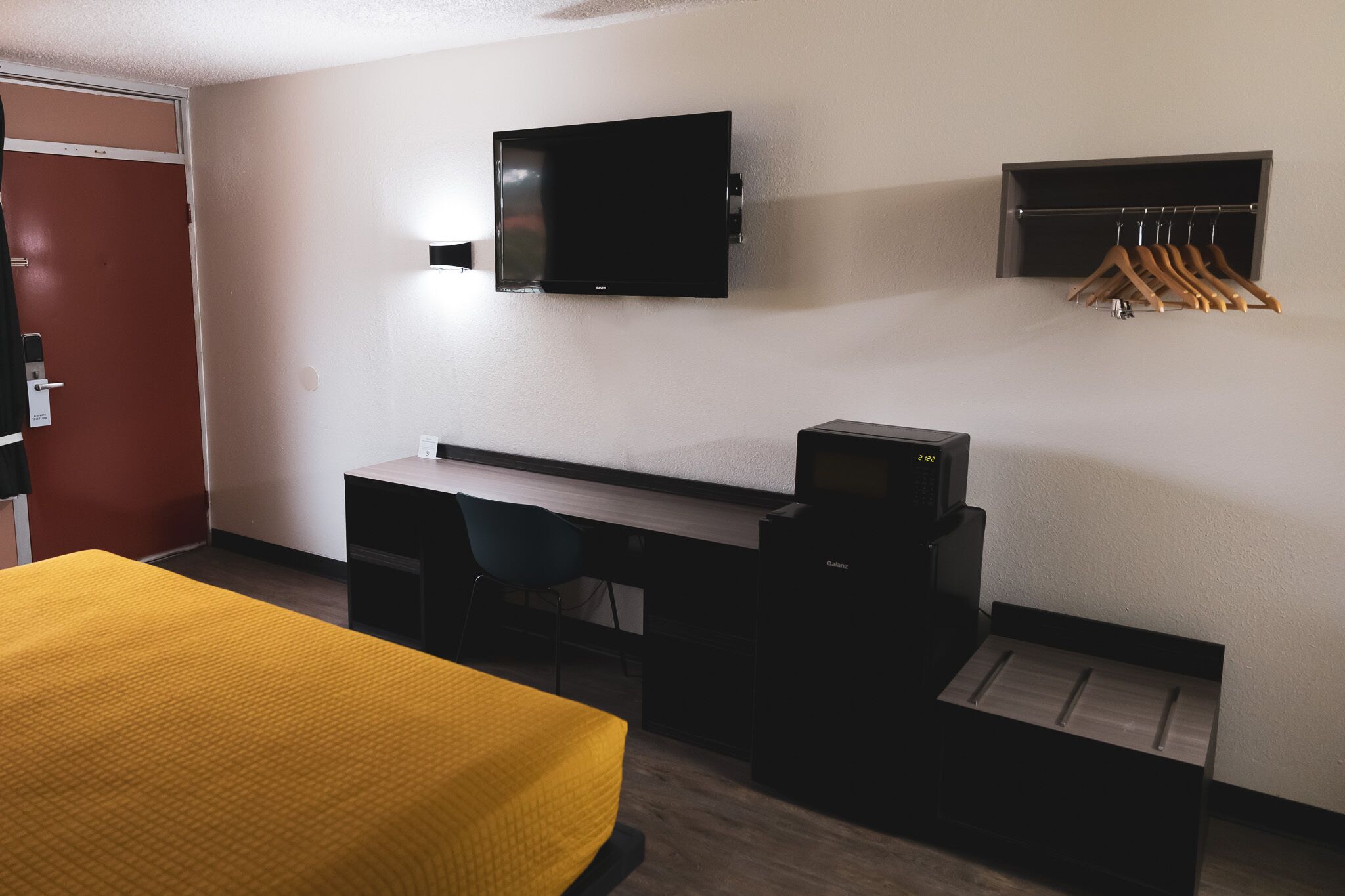 A hotel room with a bed, desk, chair, television, and a coat rack.