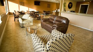 Un hall d’hôtel avec un canapé en cuir marron, des fauteuils à motifs et un coin repas comprenant des tables et des chaises.