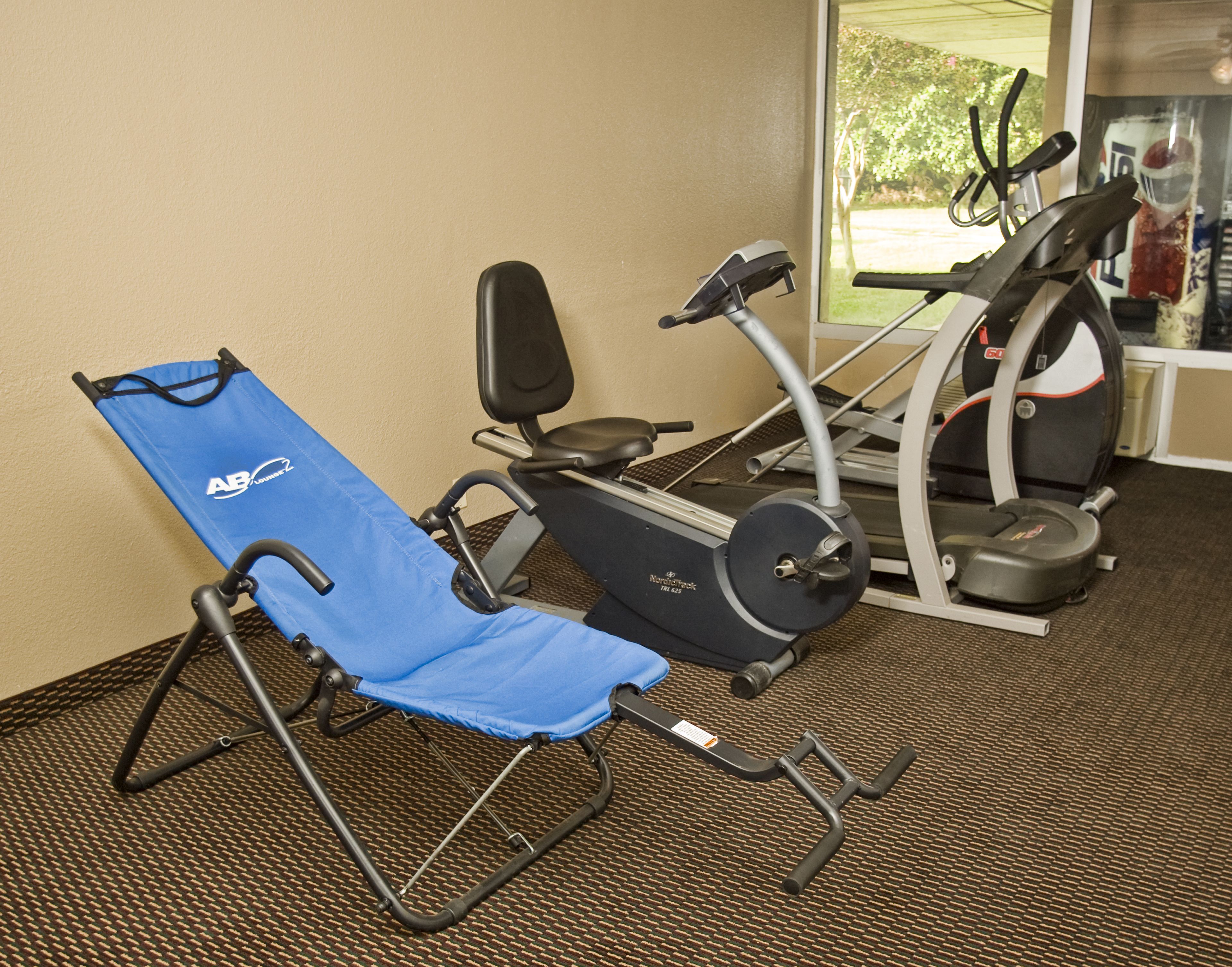A gym with exercise equipment including a stationary bike, a treadmill, and a blue exercise chair.