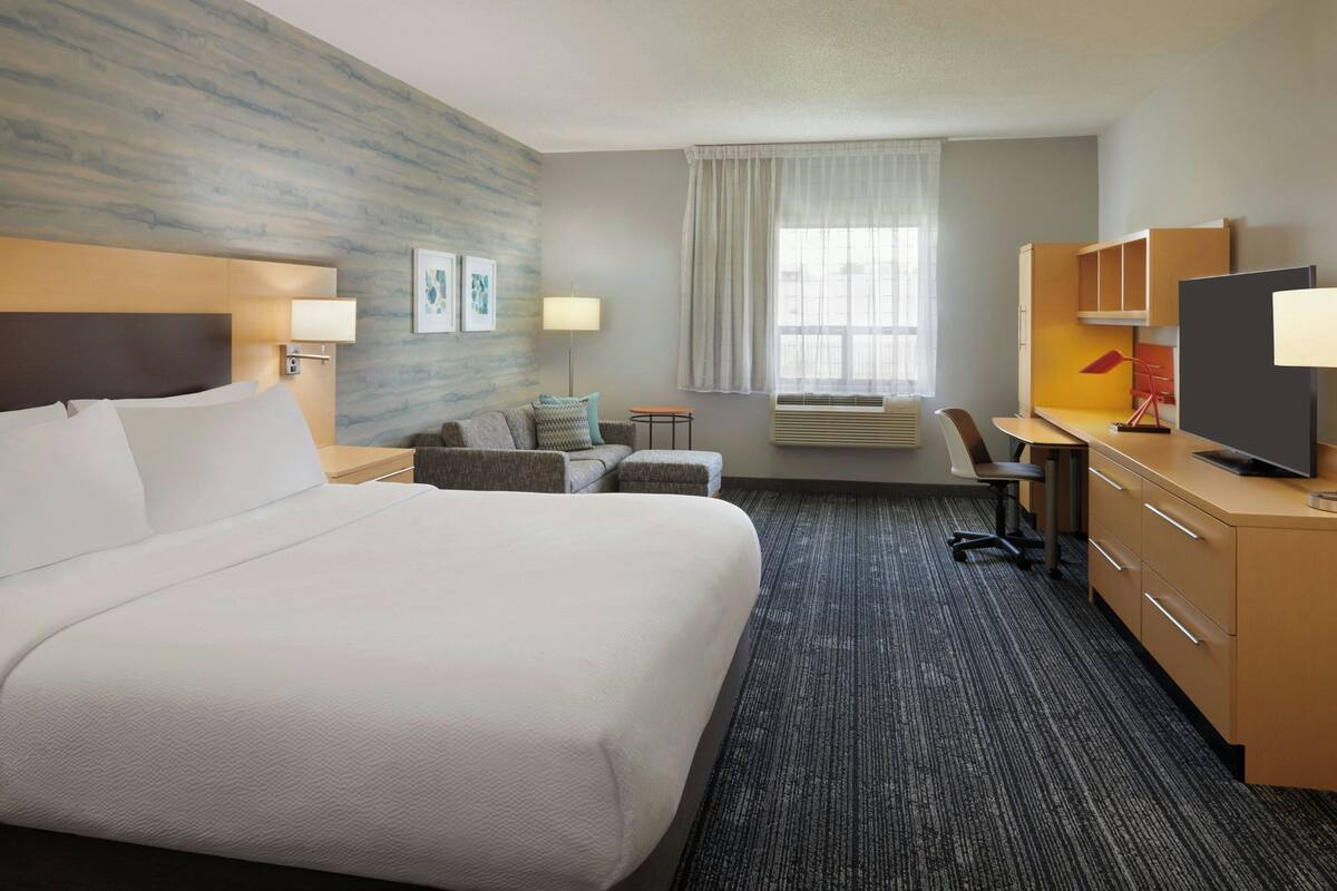 A hotel room with a large bed, a desk with a computer, a chair, and a TV.