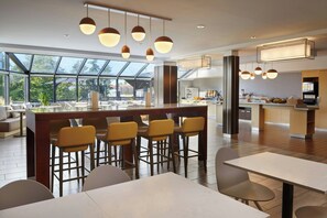 A modern restaurant with a bar area, high ceilings, and large windows offering views of the outdoors. - TownePlace Suites by Marriott London (London)