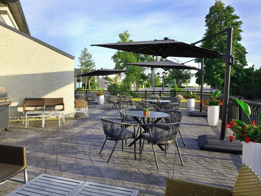 Área de terraço ao ar livre com mesas, cadeiras, churrasqueira e guarda-sóis para proteção do sol.