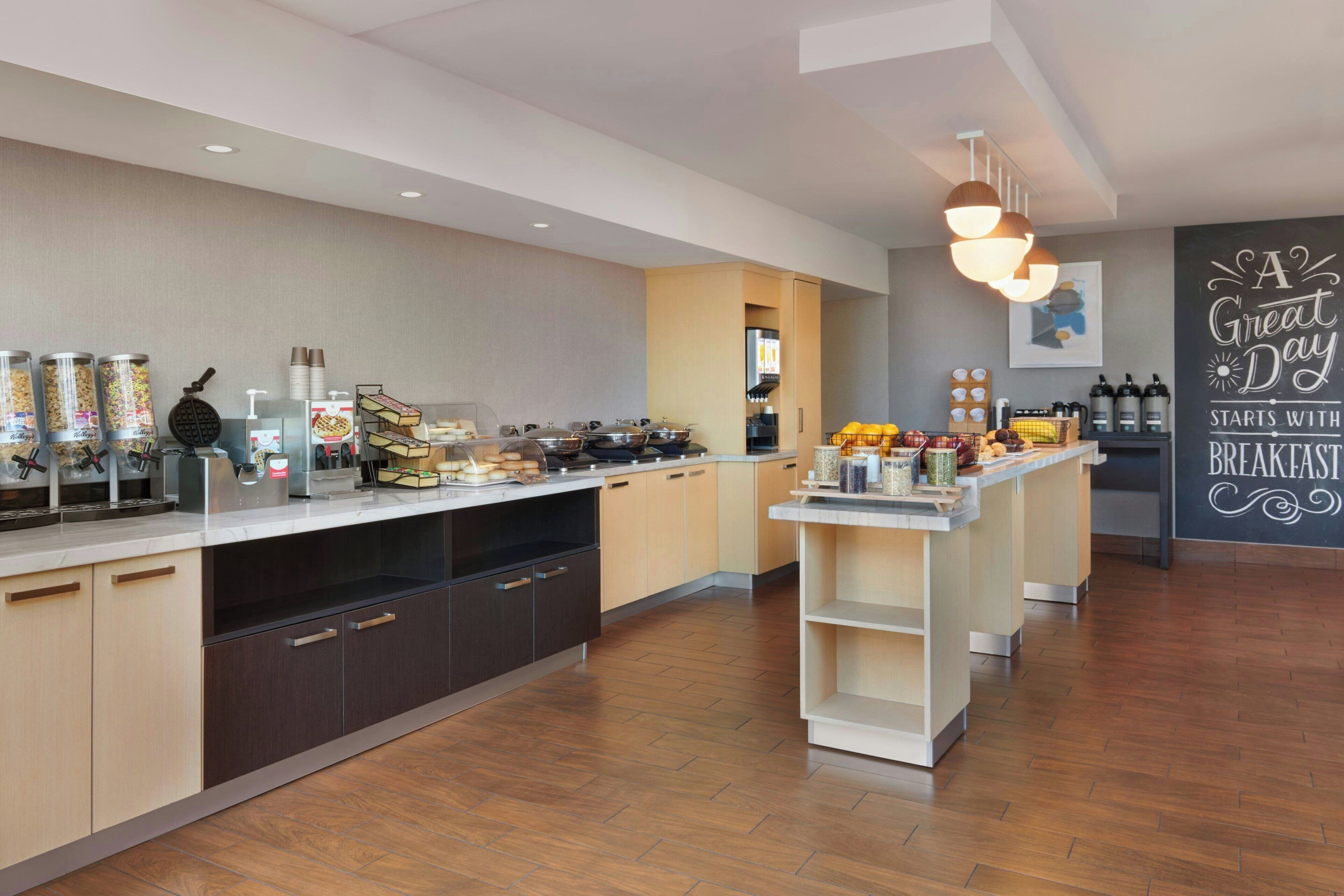 A modern breakfast bar with a variety of food items and beverages, wooden flooring, and a motivational wall quote.
