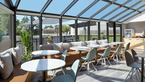 A modern outdoor dining area with a glass roof, cushioned seating, and round tables. - TownePlace Suites by Marriott London (London)