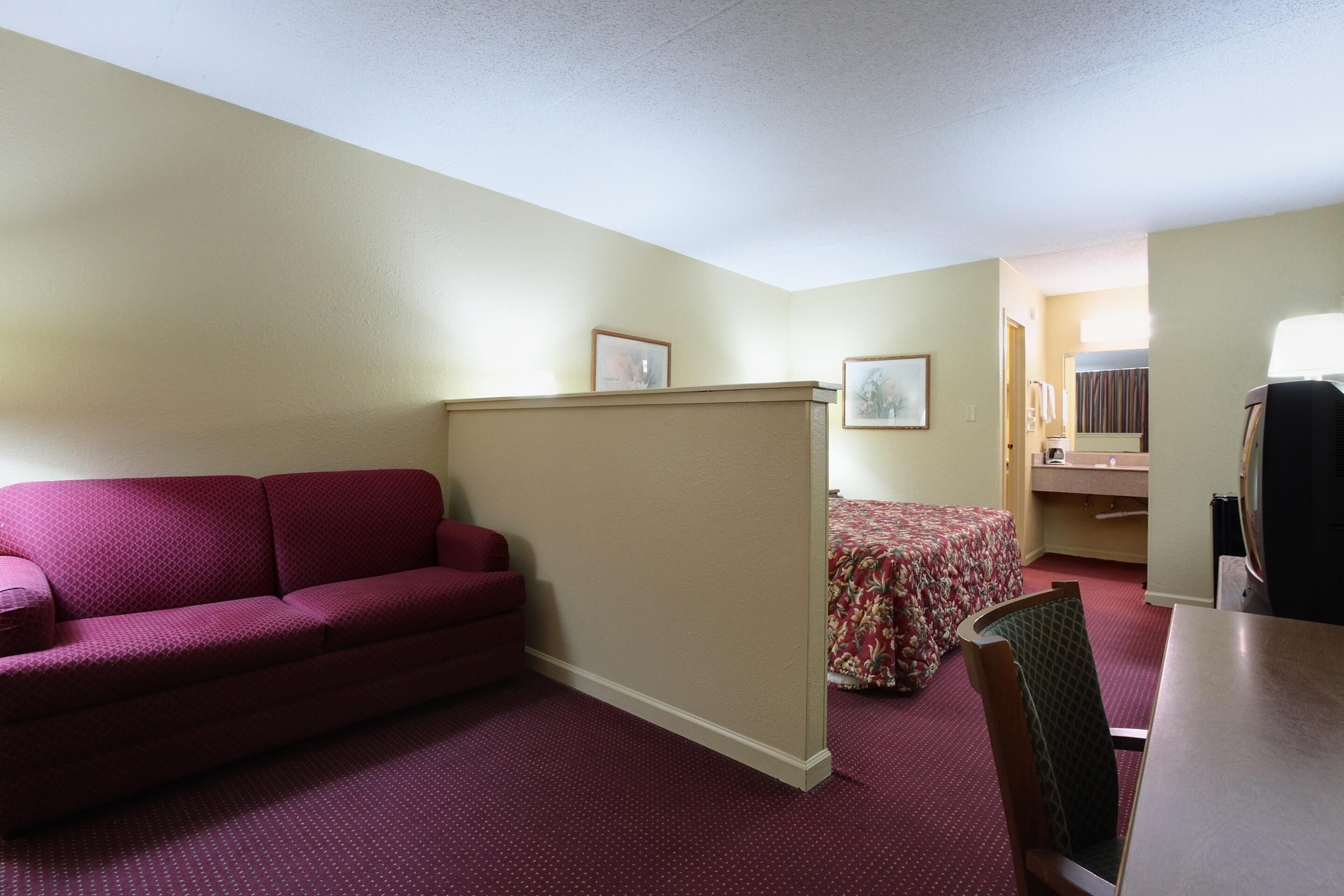 A hotel room with a red sofa, a bed with floral bedding, a small table, and a television.