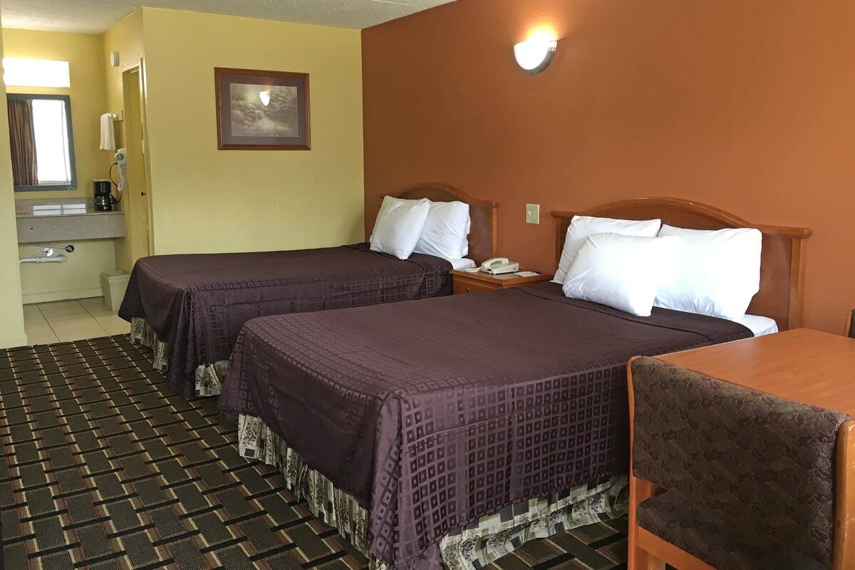 Hotellihuone, jossa on kaksi sänkyä, kylpyhuone ja pieni pöytä.