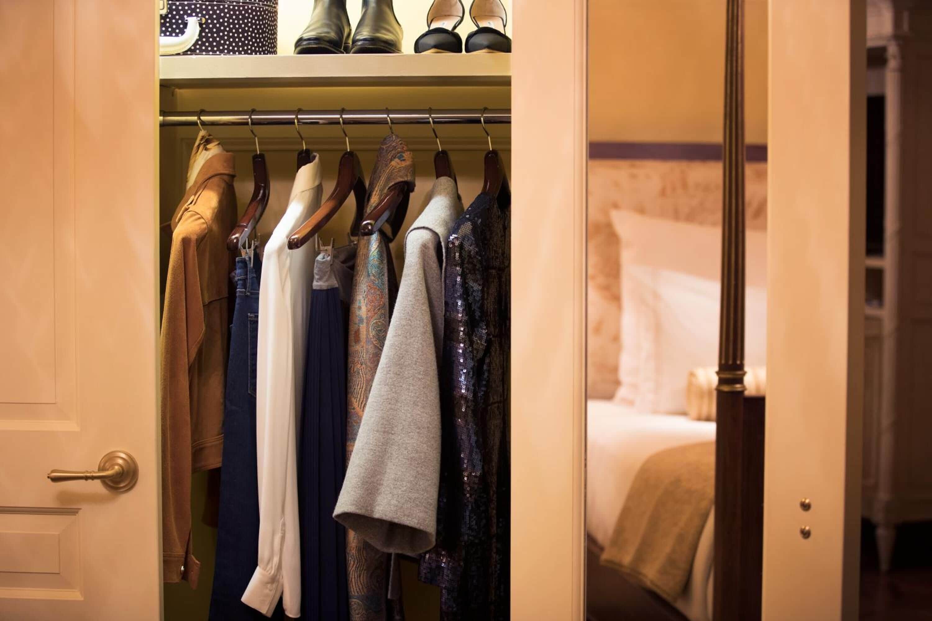 A hotel room with a closet containing various clothing items.