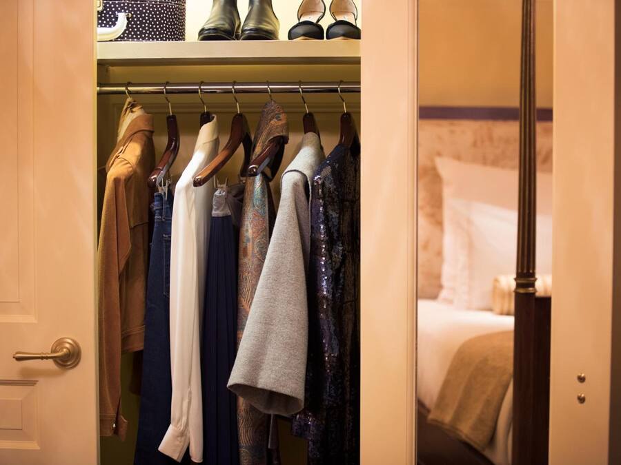 A hotel room with a closet containing various clothing items.