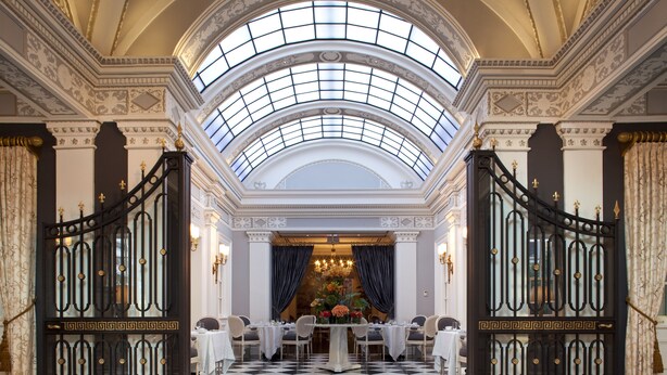 An opulent room with a high arched skylight, a checkered floor, and a formal dining setup with a floral centerpiece.