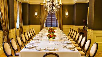 A formal dining room with a long table set for a meal, flanked by chairs, a chandelier, and patterned carpet.