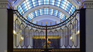 A grand entrance with a glass dome ceiling, ornate metal gates, and a checkered floor.