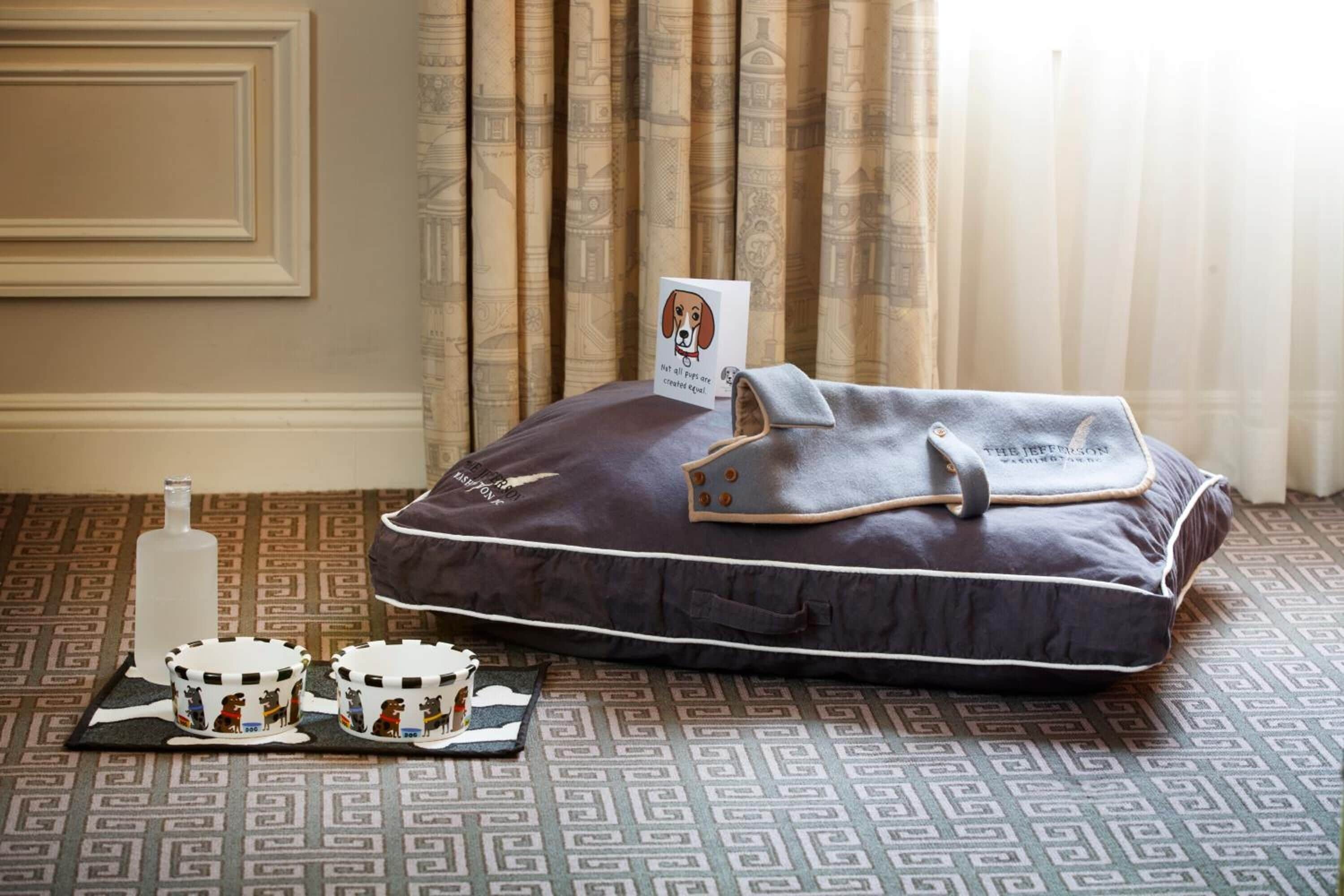 Una habitación con alfombra estampada, un bolso de cuero oscuro con una etiqueta y dos tazas con ilustraciones de perros.