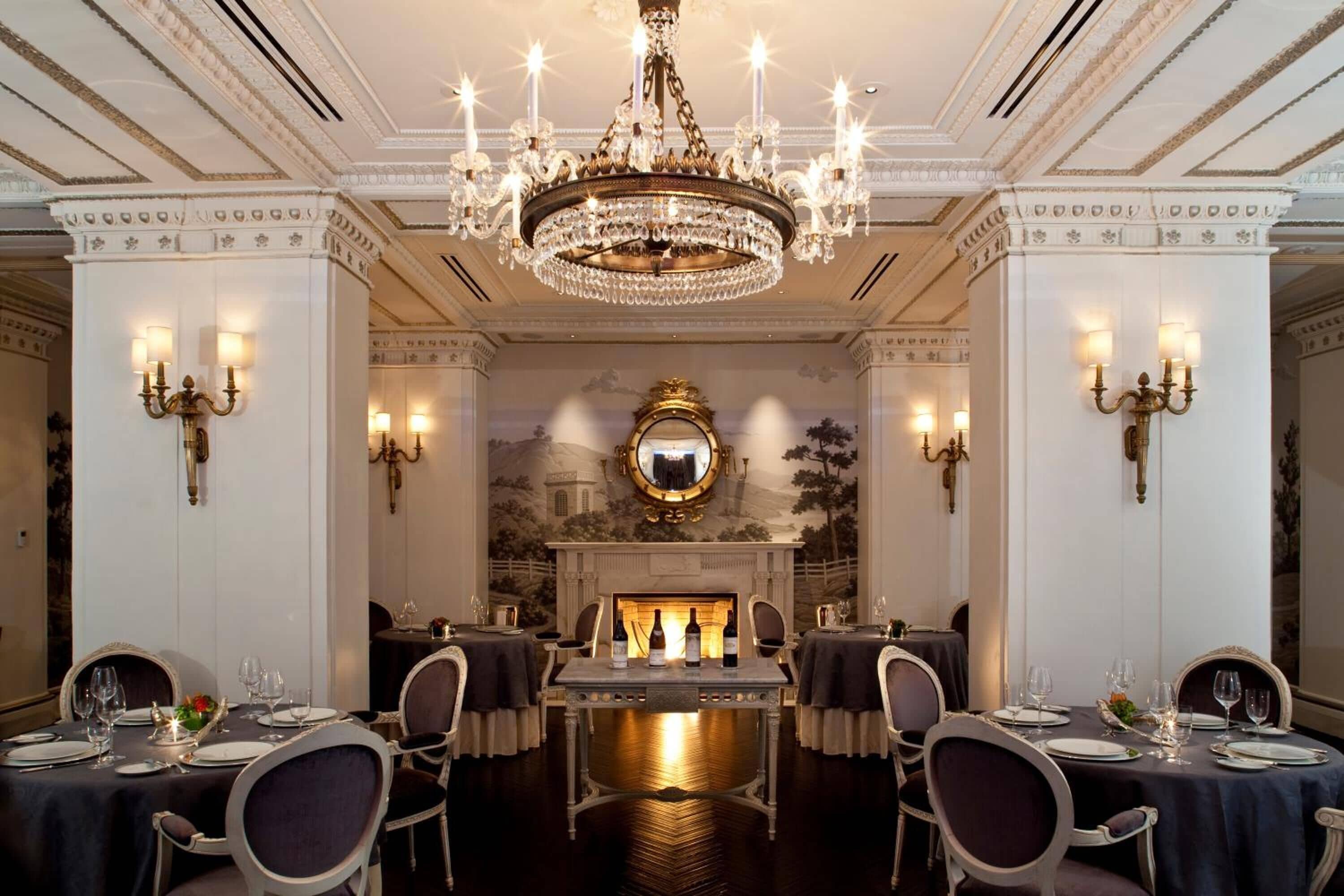 A formal dining room with a chandelier, fireplace, and classical decor.