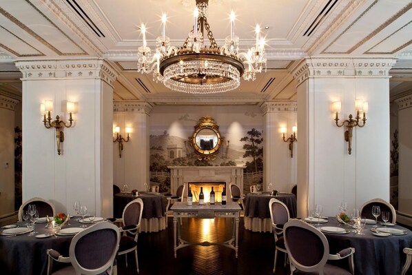 A formal dining room with a chandelier, fireplace, and classical decor.