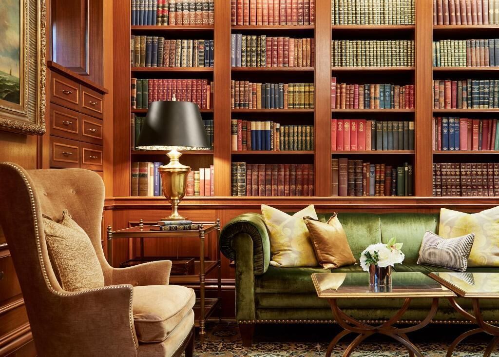 Een bibliotheek met boekenplanken, een groene bank, een stoel en een lamp.
