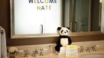 A bathroom with a mirror, two sinks, a panda plush toy, and a welcome sign.