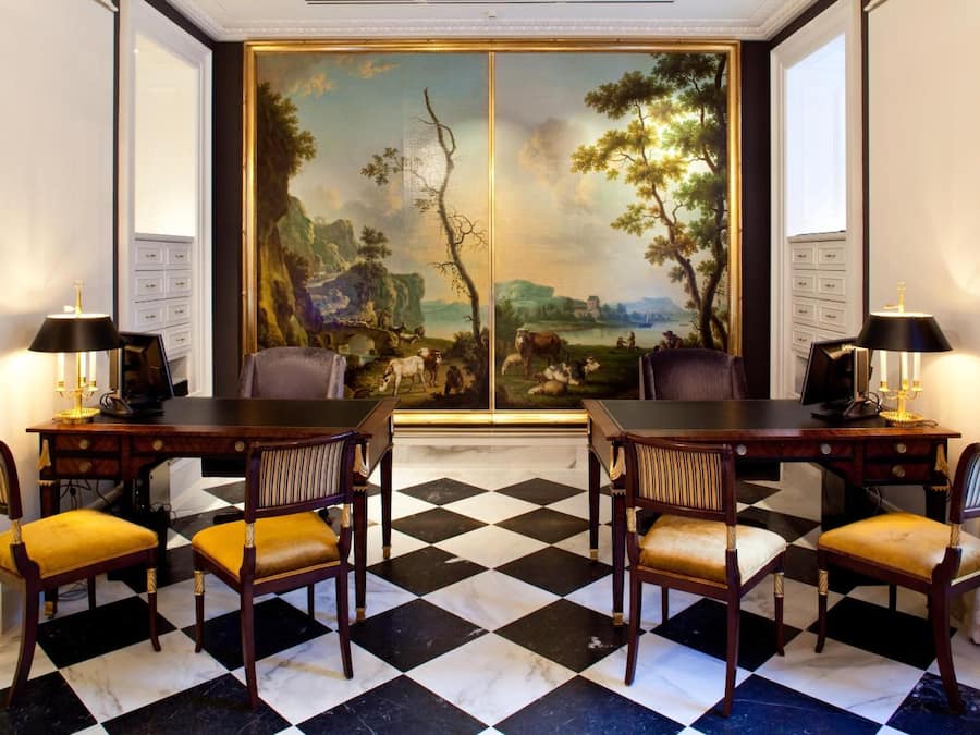 Comedor con piso a cuadros, un cuadro grande de paisaje y una mesa para cuatro con sillas.