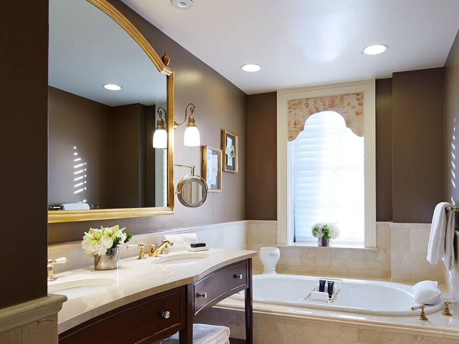 A bathroom with a large mirror, two sinks, a bathtub, and a window with blinds.