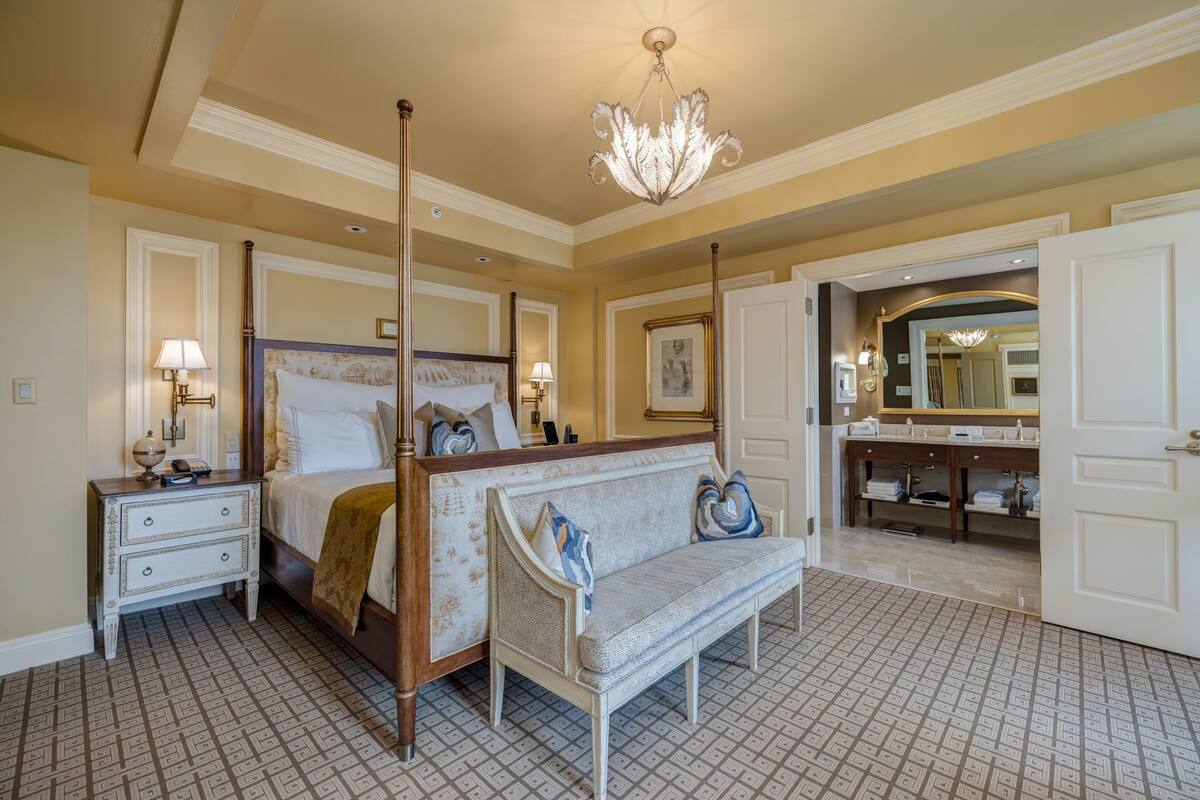 A four-poster bed with a canopy, a bench, a nightstand, and a vanity with a mirror.