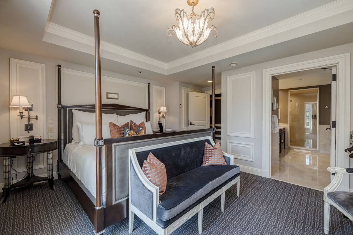 A spacious bedroom with a four-poster bed, a dark blue sofa, and a chandelier.