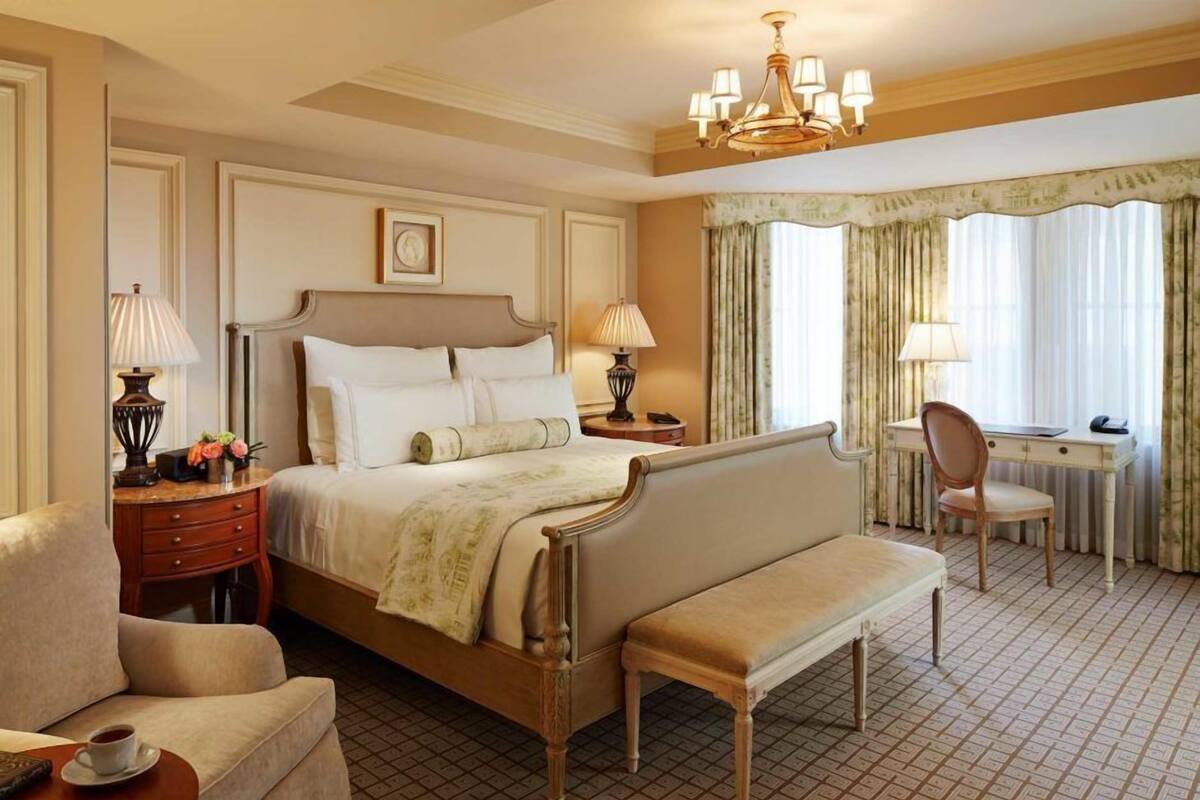 A hotel room with a large bed, a desk, a chair, a bench, and two bedside tables with lamps.