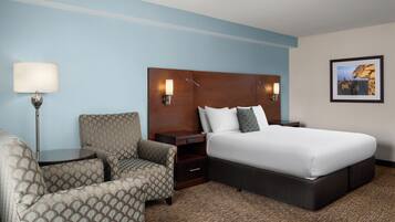 A hotel room with a bed, a chair, a nightstand, and a lamp.
