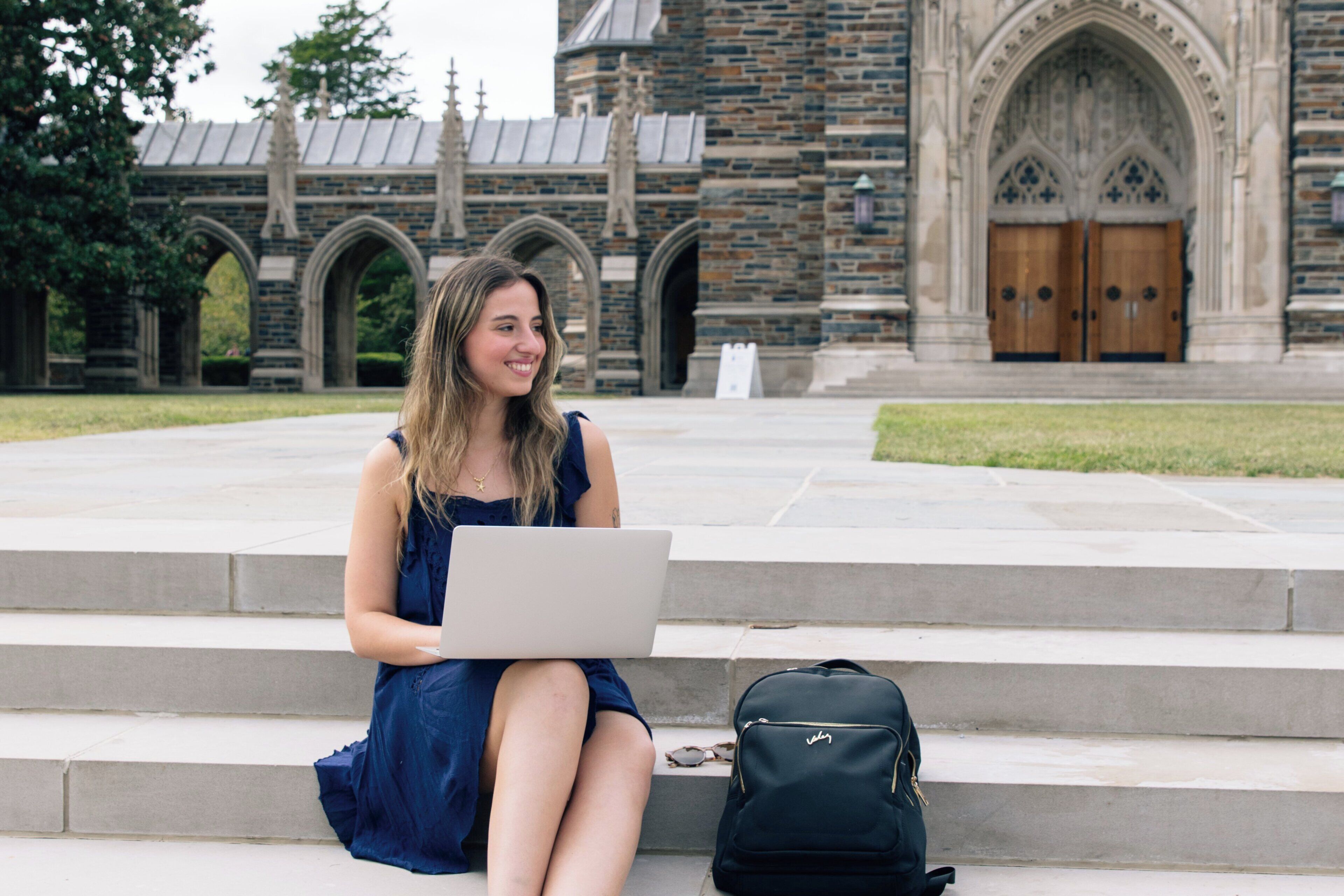 A person sitting on steps with a laptop and a backpack.