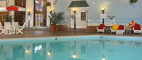 A pool area with lounge chairs, a small building with a sign, and a mural of a beach scene.