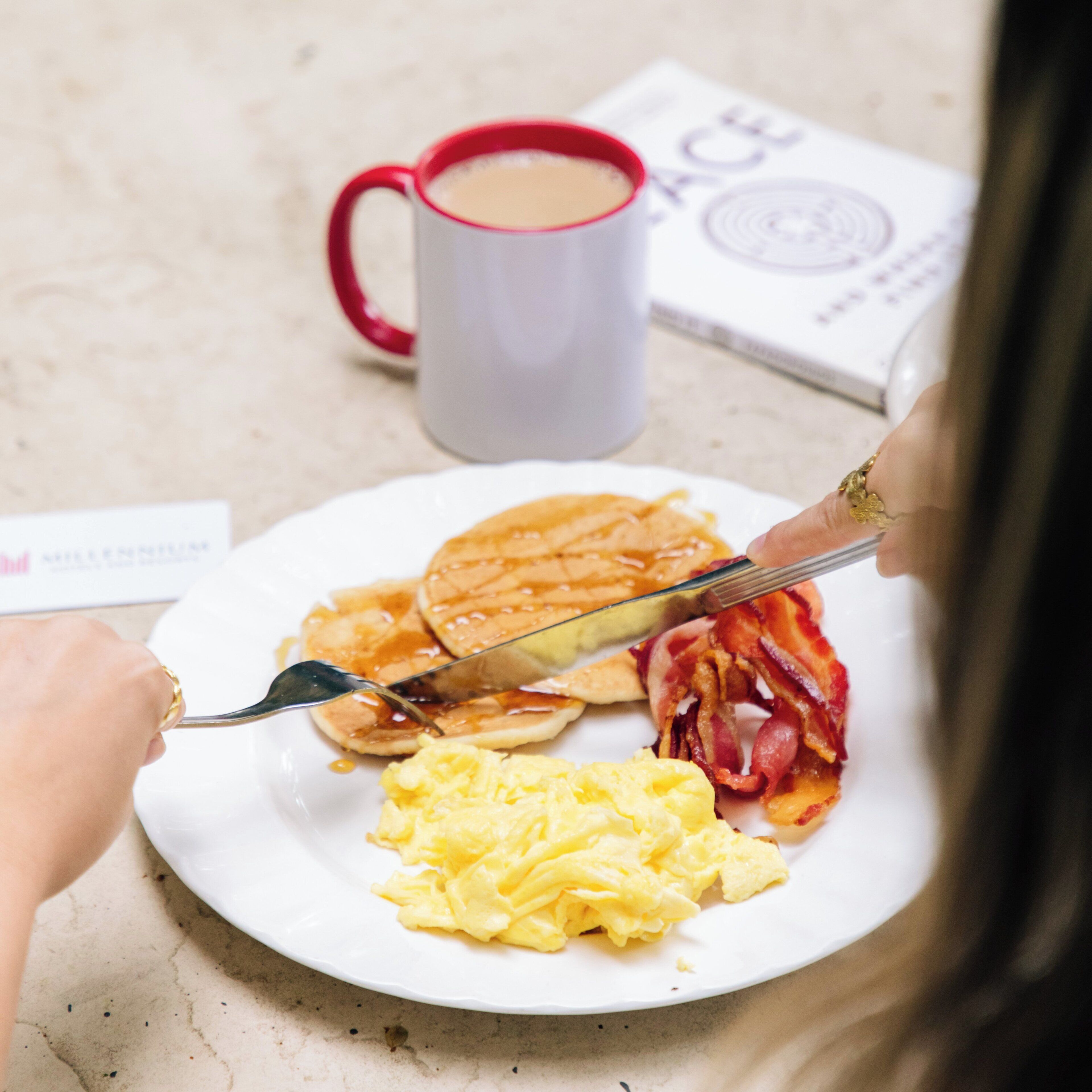 A breakfast plate with pancakes, bacon, and scrambled eggs.