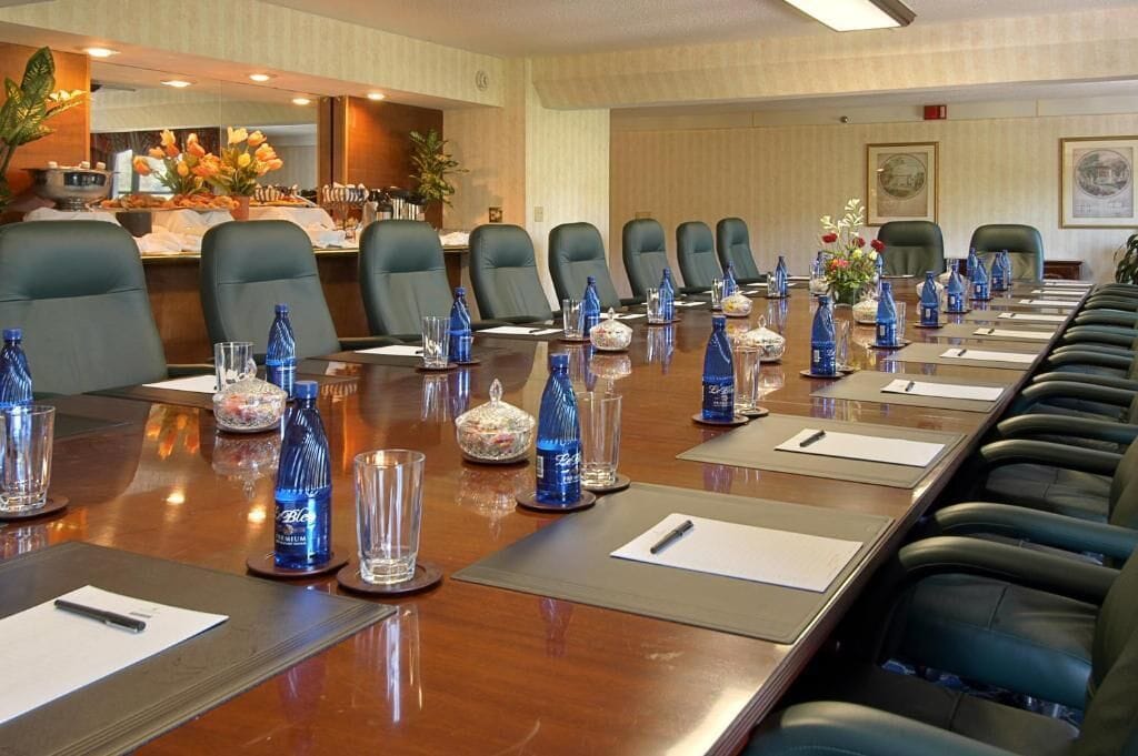 A conference room with a long table, multiple chairs, water bottles, and a buffet area in the background.