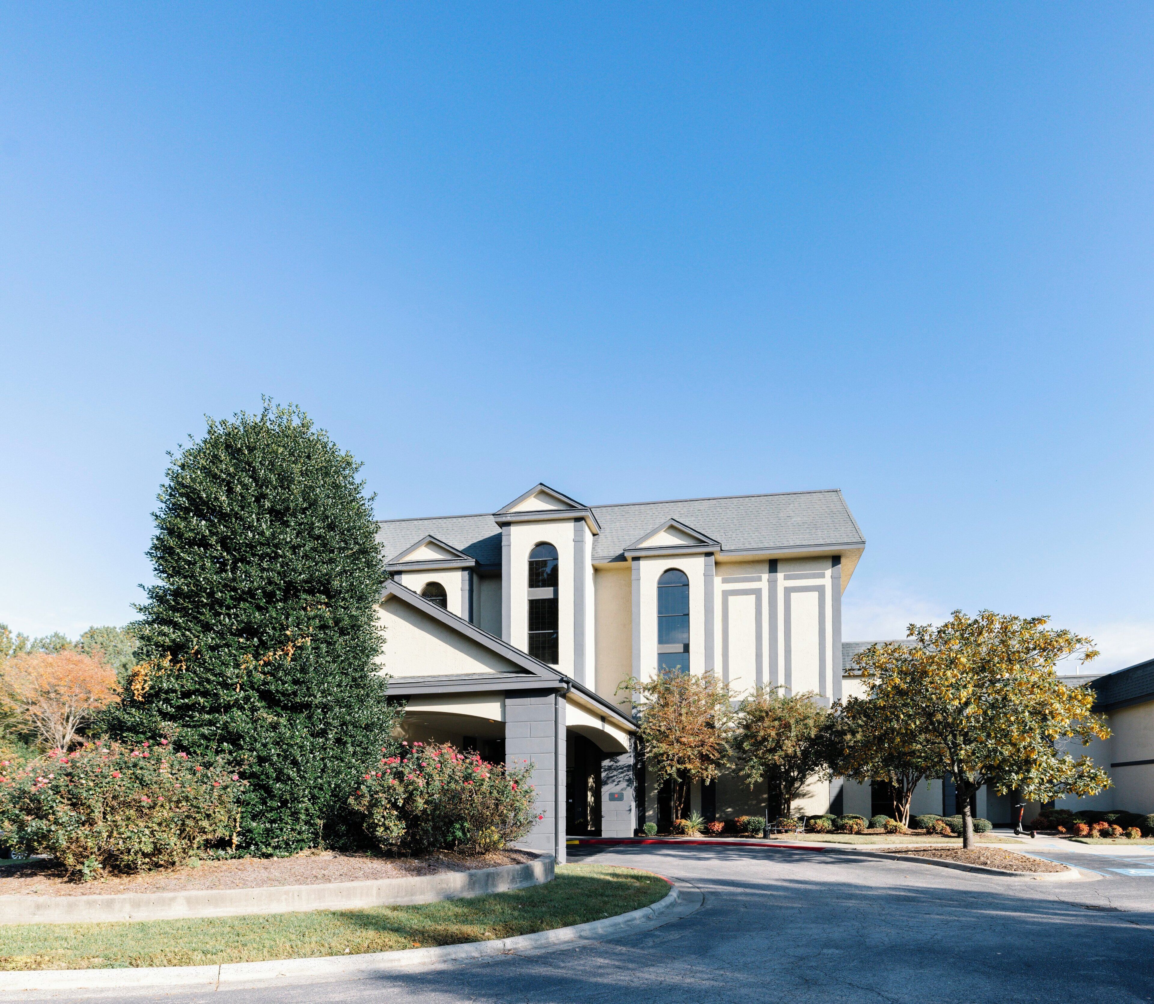 A two-story house with a covered driveway, a large tree, and a well-maintained lawn.