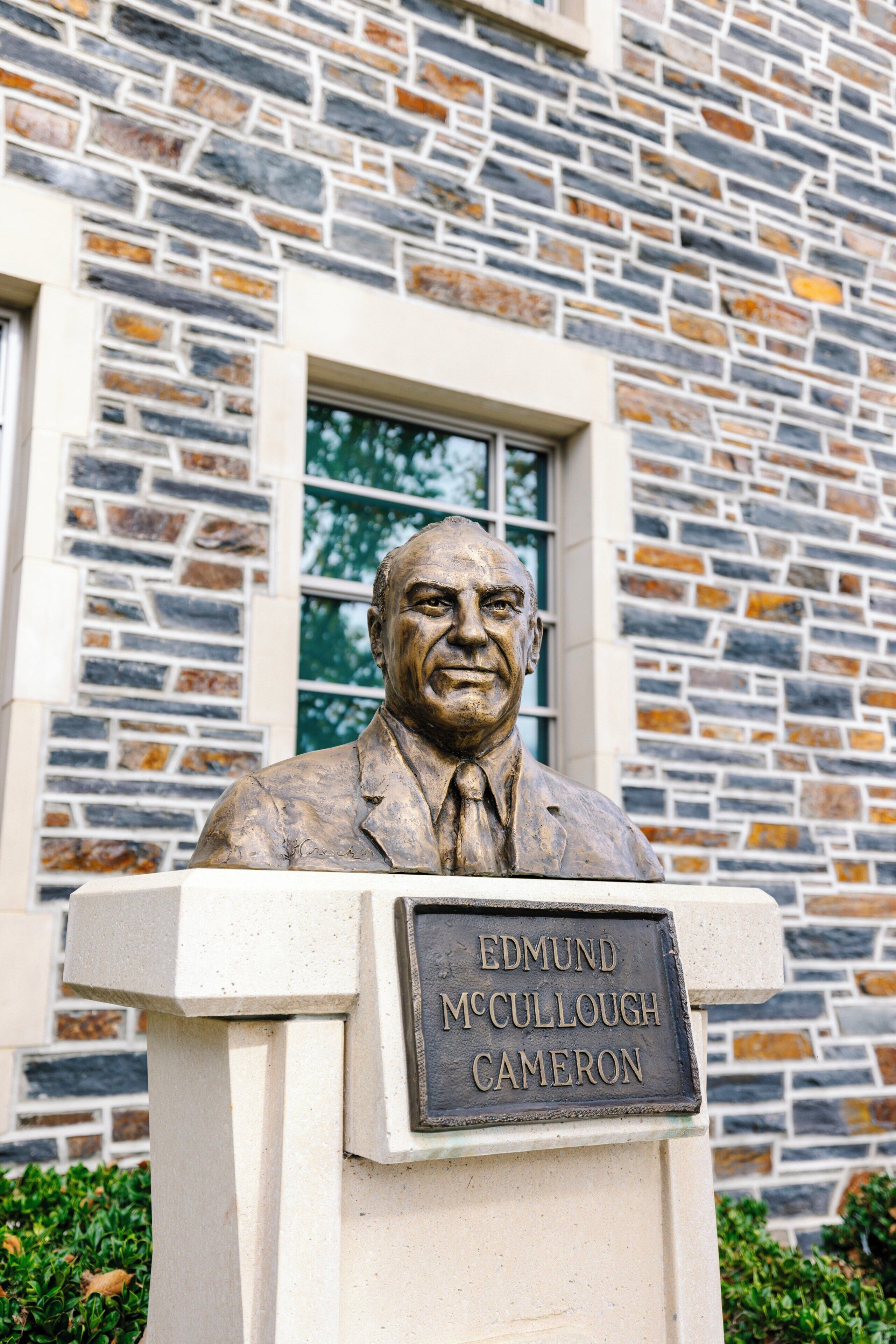A statue of Edmund McCullough Cameron with a plaque, set against a stone building facade.
