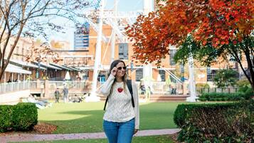 A woman walking on a pathway with autumn foliage and a white structure in the background.