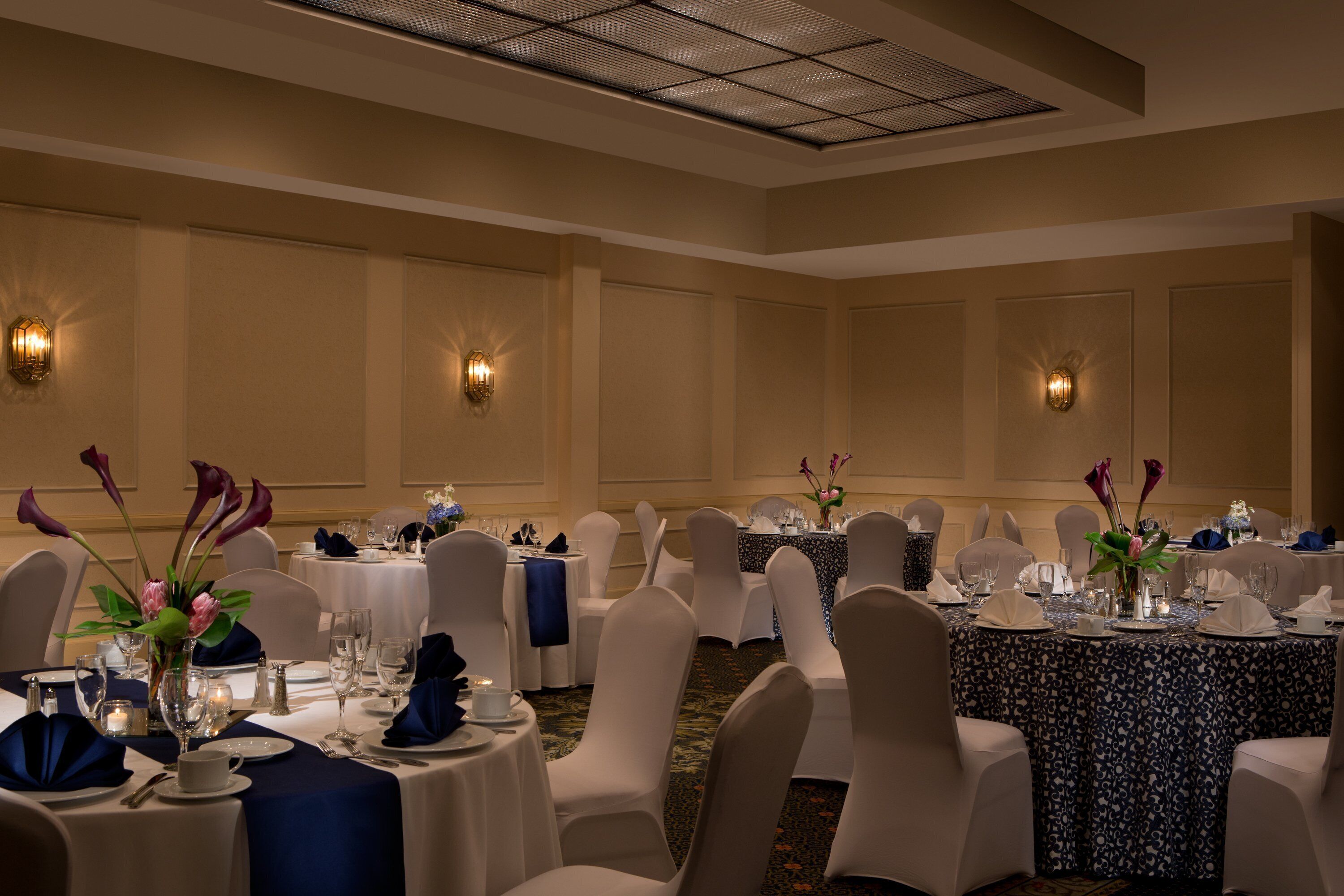 A banquet hall with round tables, white chairs, and floral centerpieces.