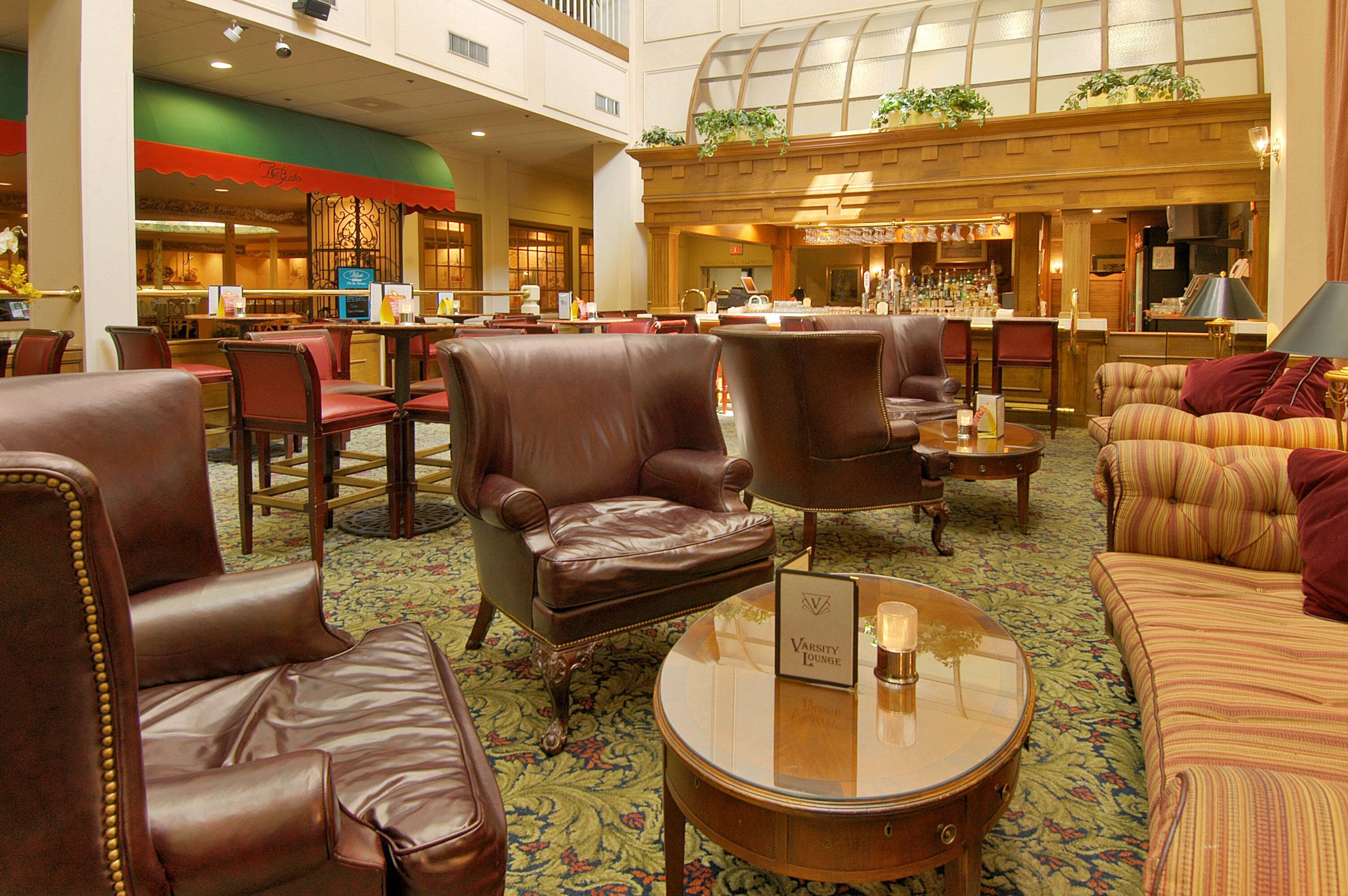 A hotel lobby with leather chairs, a round coffee table, and a bar area in the background.