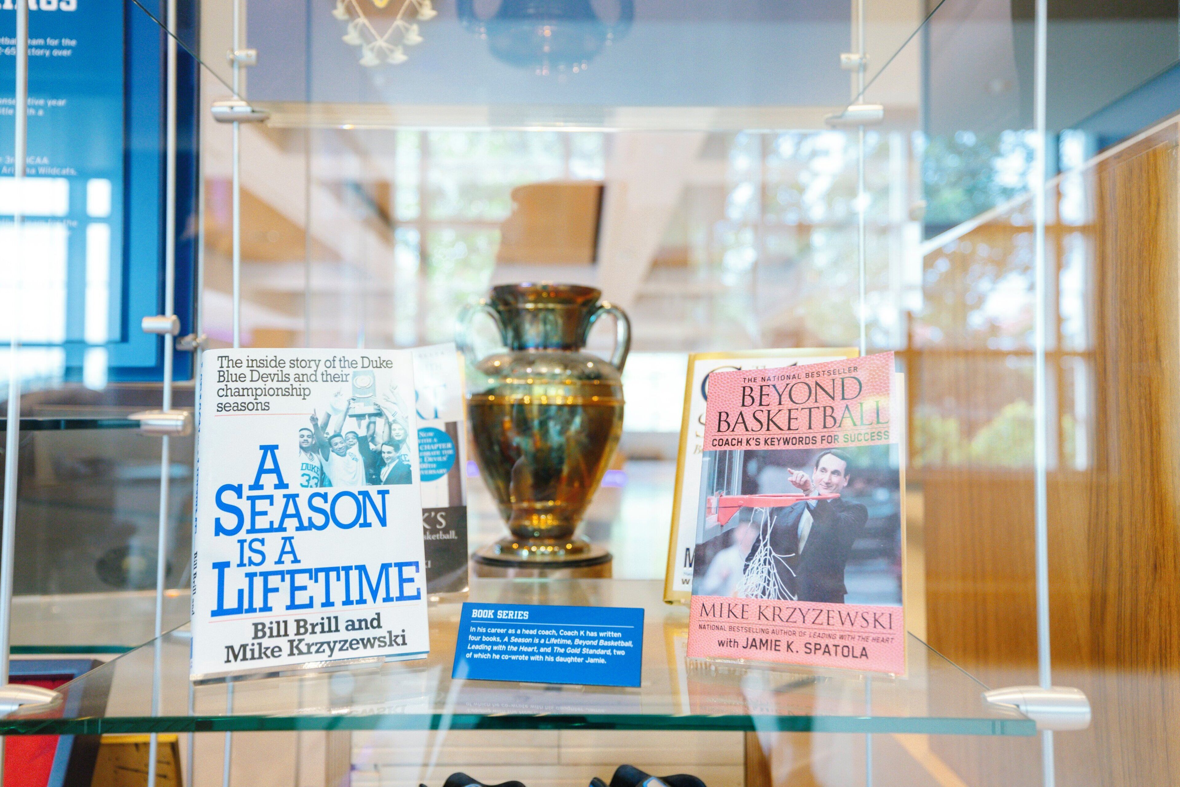 Una vitrina de vidrio con un trofeo y dos libros titulados 'A Season is a Lifetime' y 'Beyond Basketball'.