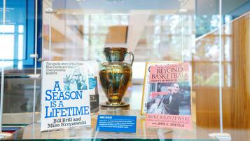 Una vitrina de vidrio con un trofeo y dos libros titulados 'A Season is a Lifetime' y 'Beyond Basketball'.