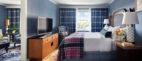 A bedroom with a bed, a television, a dresser, a window with curtains, and a nightstand with a lamp.