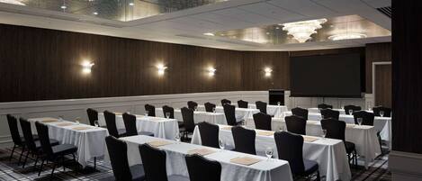 A conference room with rows of tables and chairs, a large screen, and a chandelier.