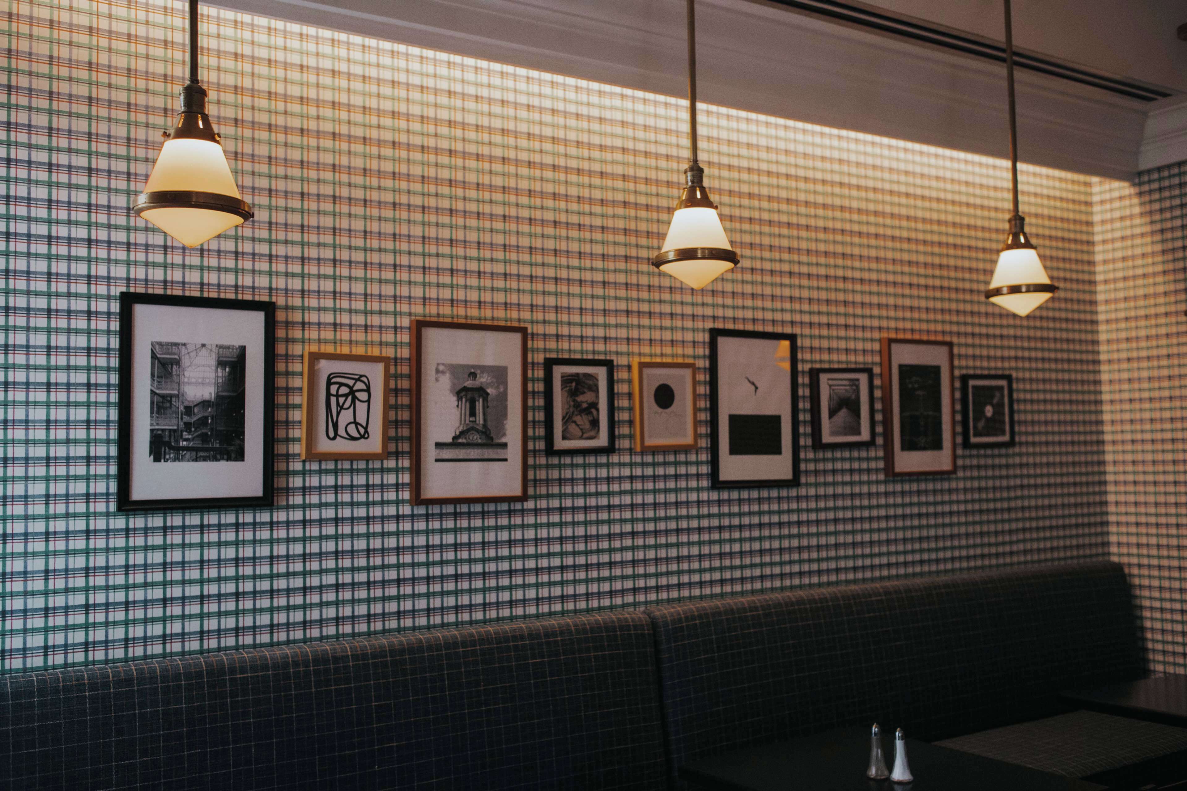 Ein Restaurantinnenraum mit karierter Wand, gerahmten Kunstwerken und hängenden Pendelleuchten.