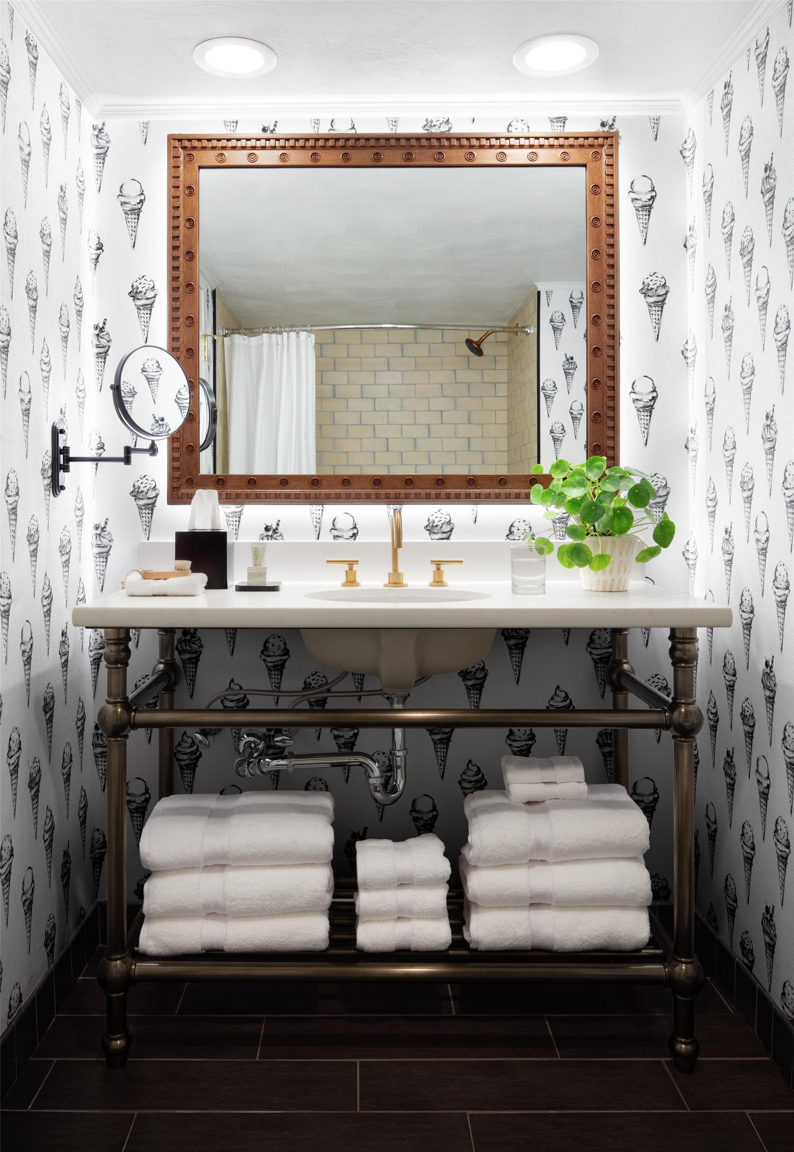 Une salle de bain avec un lavabo blanc, un miroir avec un cadre en bois et un porte-serviettes sur lequel sont pliées des serviettes.