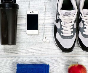 A pair of Nike sneakers, a smartphone, earphones, a water bottle, a towel, and an apple on a wooden surface. - Graduate by Hilton State College (State College)