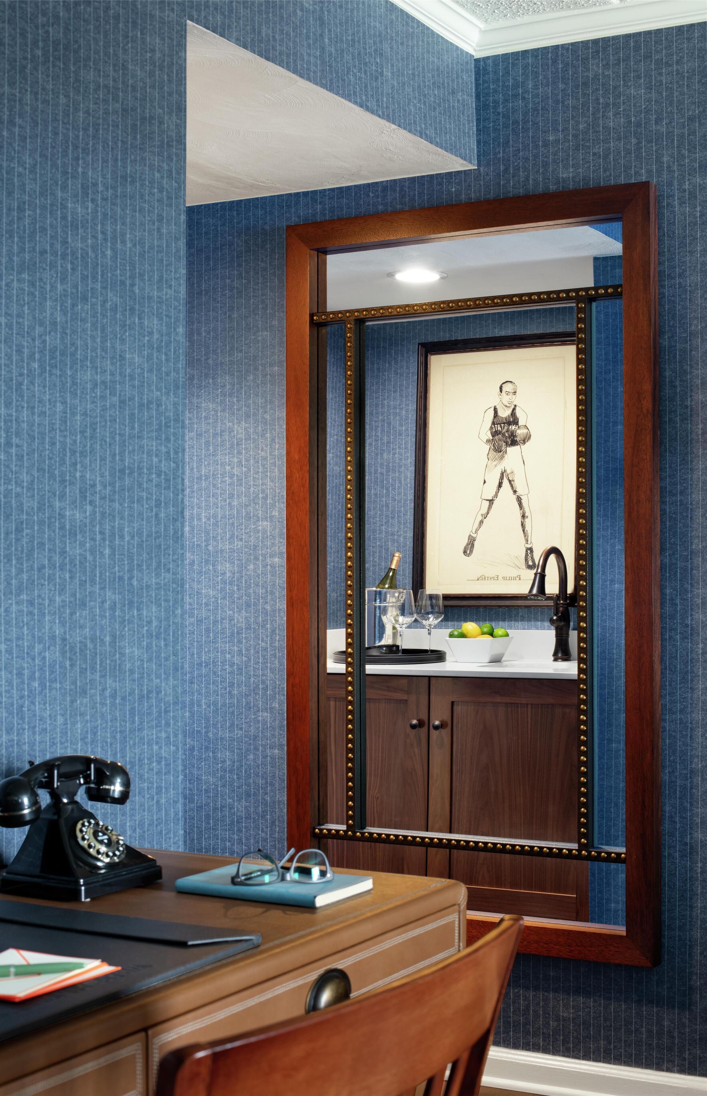 Una habitación con escritorio de madera, teléfono, cuadro enmarco y espejo con marco decorativo.