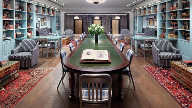 Un salón de reuniones formal con una larga mesa, sillas, estanterías y una araña.