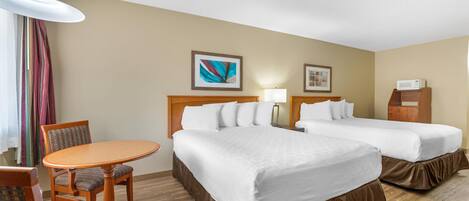 A hotel room with two beds, a desk, a chair, a lamp, and artwork on the walls.