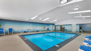 Ein Hallenbad mit blauem Wasser, umgeben von Liegestühlen und einem Wandgemälde eines Segelboots.