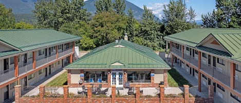 A motel with a central building and two wings, featuring a green roof, brick facade, and a parking lot.