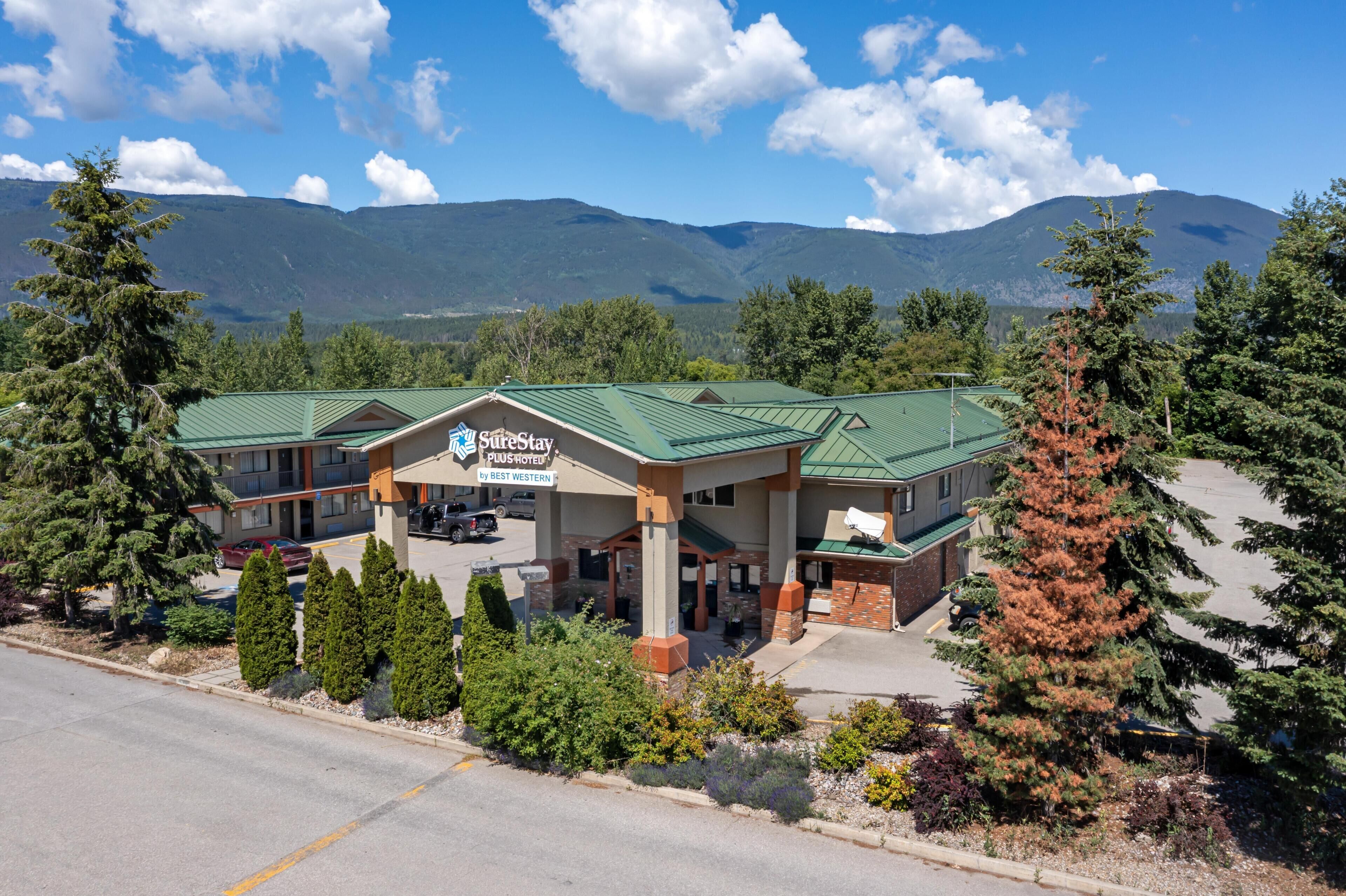 Un hotel con techo verde, un cartel que dice 'SureStay PlusHotel by Best Western' y un paisaje montañoso de fondo.