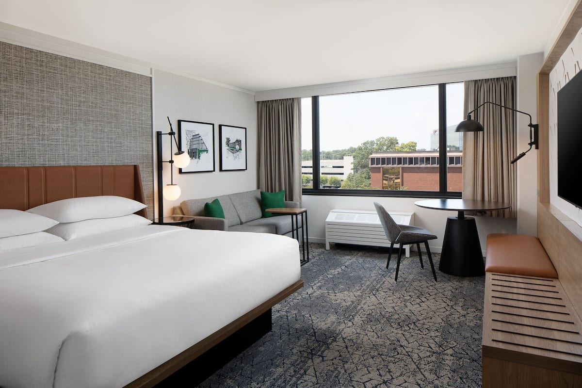 A hotel room with a large bed, a sofa, a desk, and a TV.